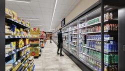 A supermarket aisle with a very long refrigerated shelf on the right, a man stands in front of it and looks for products; Copyright: Daniel Horn